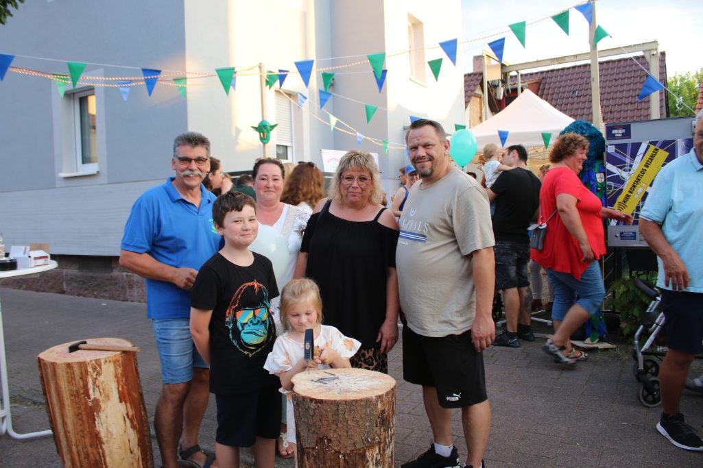 Familie und Freunde posieren lächelnd vor einem Festivalstand, umgeben von Dekoration.