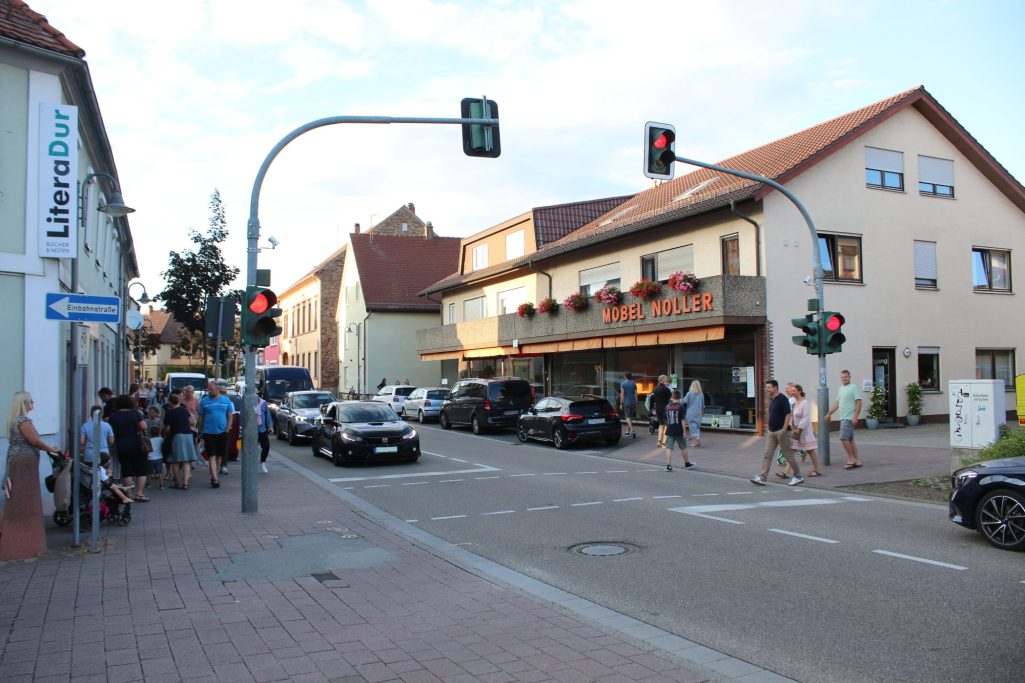 Belebte Straßenkreuzung mit Fußgängern, Ampeln und Geschäften im Hintergrund.
