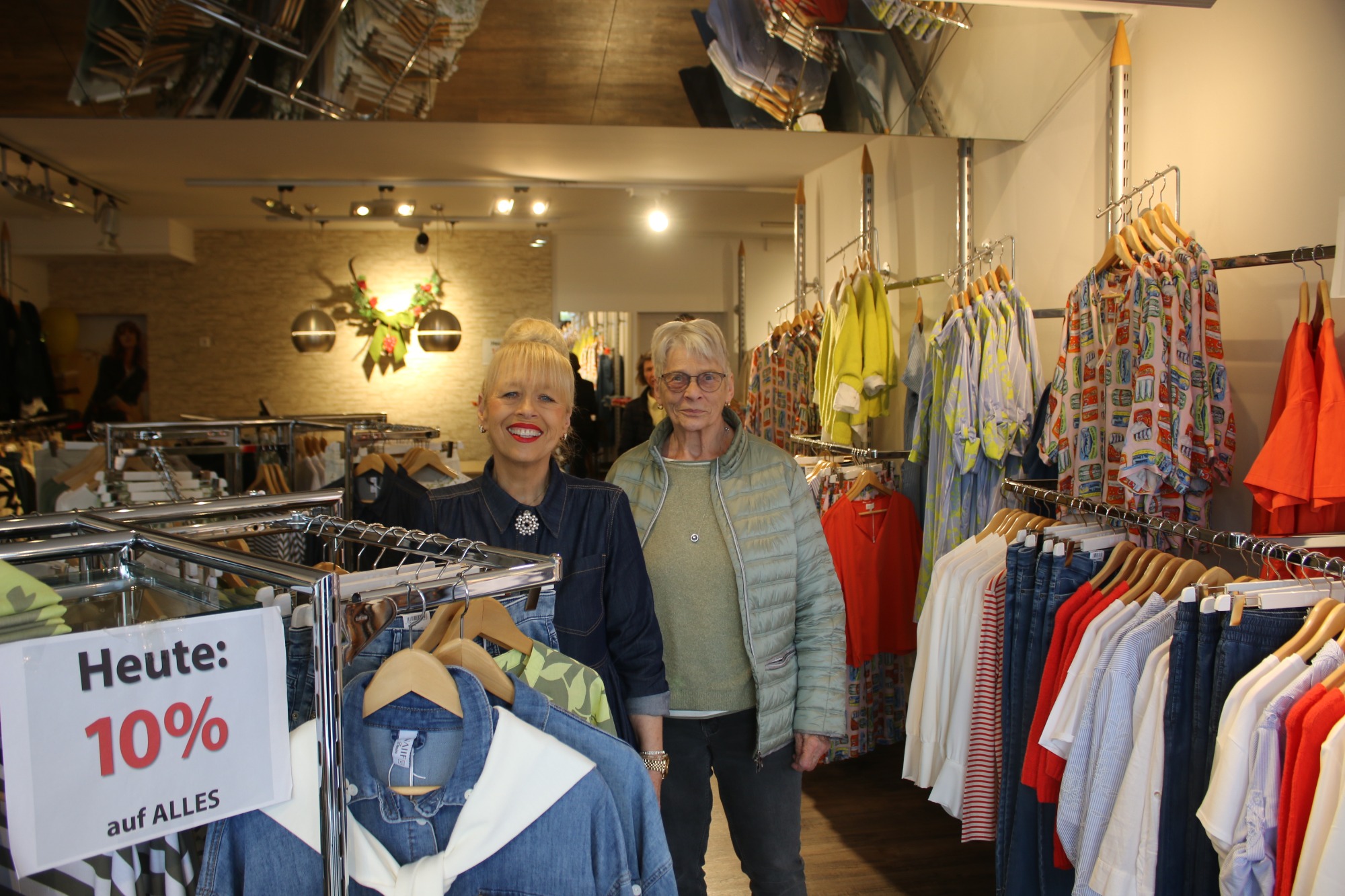 Zwei Personen in einem Bekleidungsgeschäft zwischen Regalen mit Kleidung.