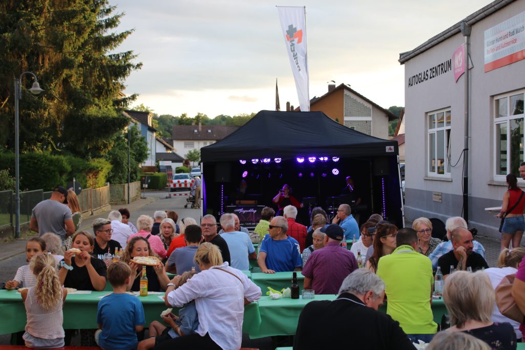 Menschen bei einer Outdoor-Veranstaltung mit Live-Musik und Festtischen.