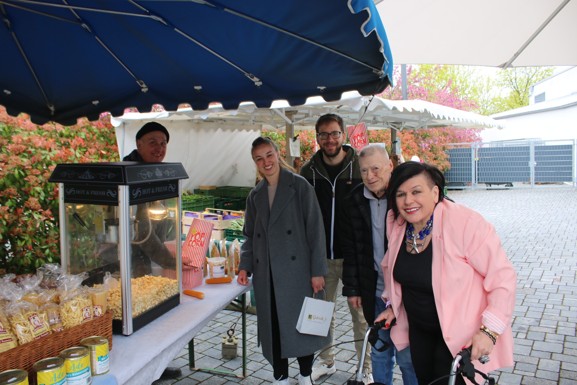 Fünf Personen stehen lächelnd vor einem Verkaufsstand mit Snacks im Freien.