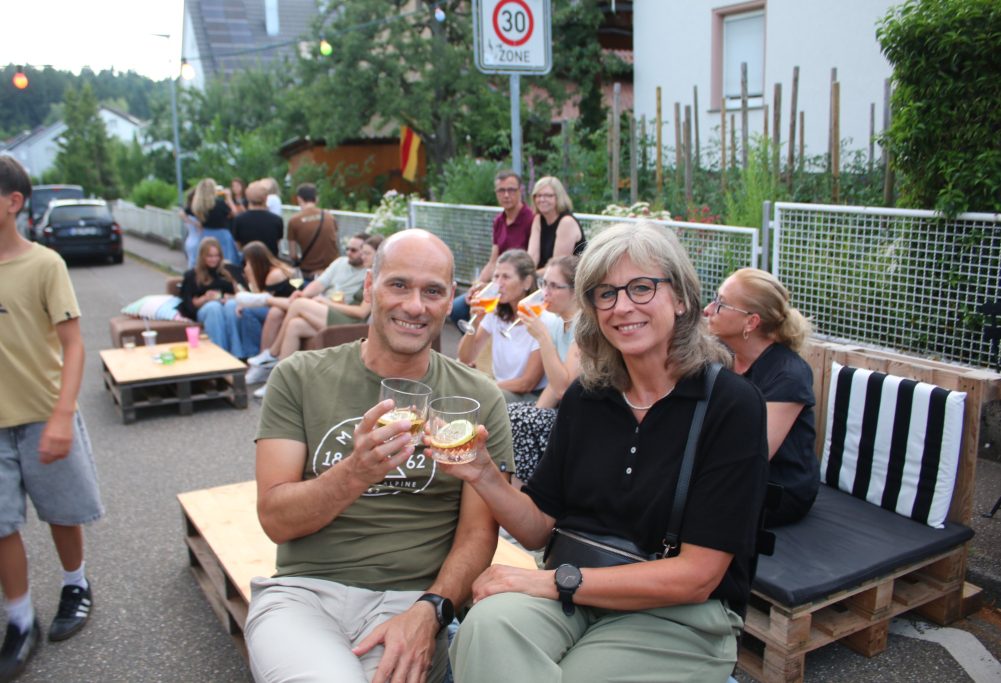 Ein Paar hält Toasts und lächelt, umgeben von Menschen auf einer Straße.