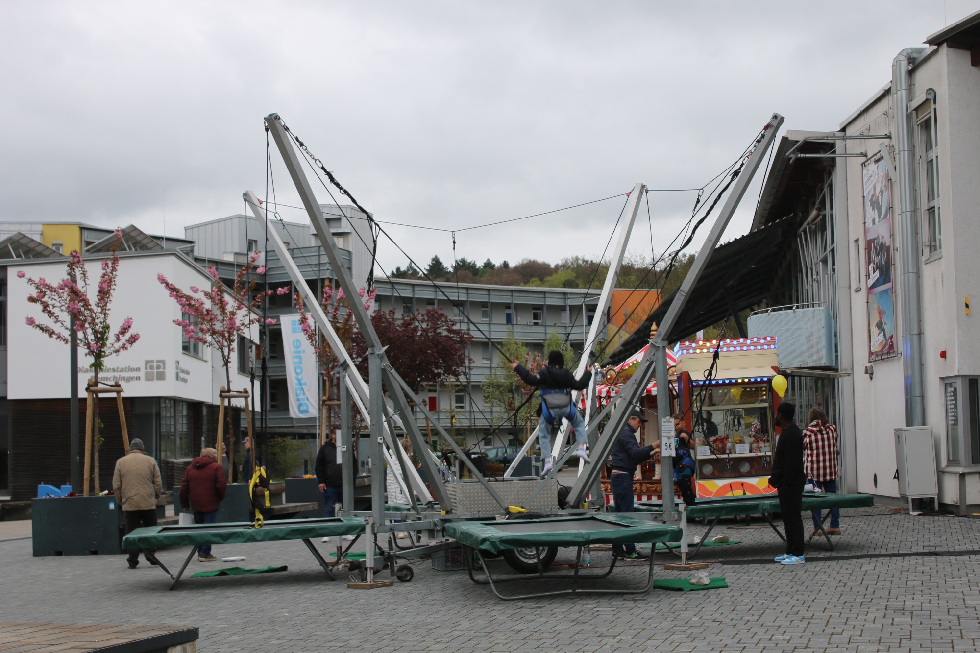 Zwei Trampoline auf einem Spielplatz mit spielenden Kindern und grauem Himmel.