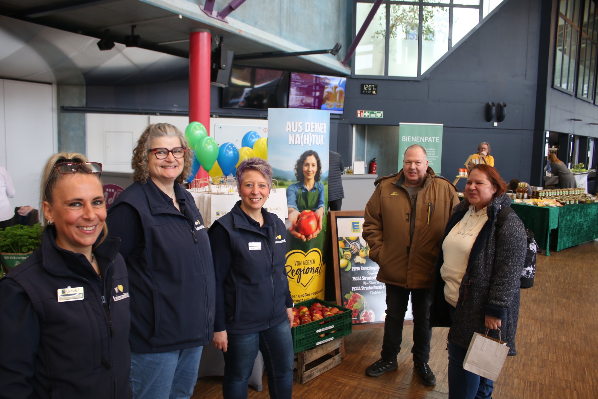 Fünf Personen stehen in einem Gebäude, umgeben von grünen Pflanzen und Dekorationen.
