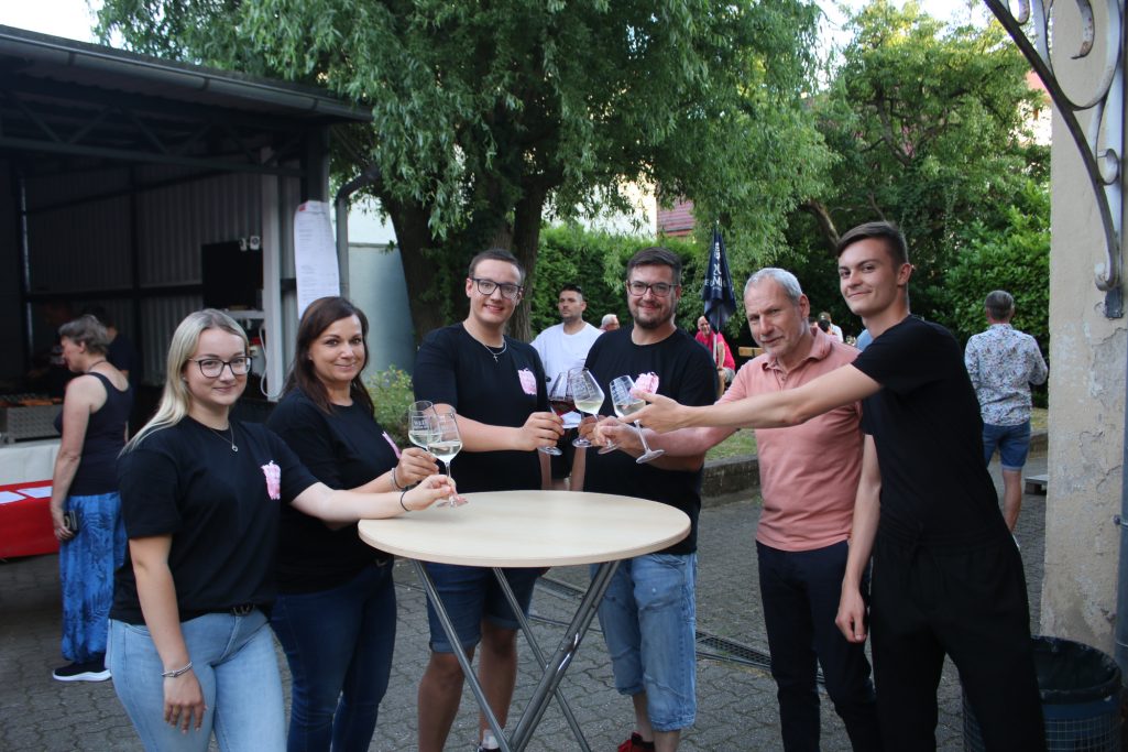 Grupp von sechs Personen in schwarzen T-Shirts an einem Tisch, lächelnd und interagierend.