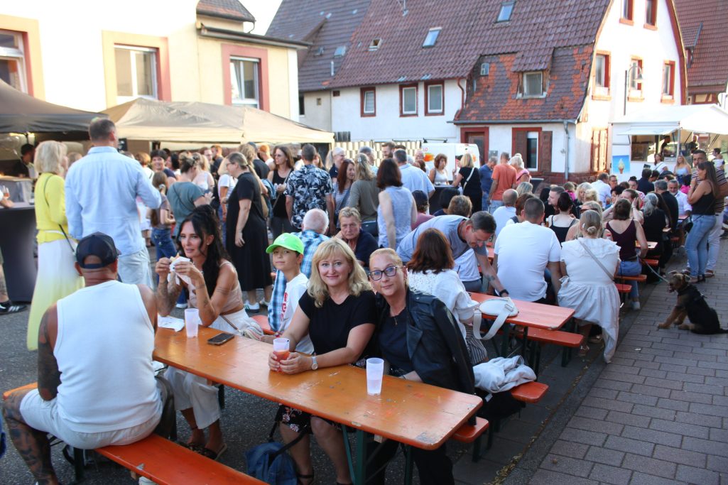 Belebtes Fest mit Menschen an langen Tischen und Ständen in einer Stadtstraße.
