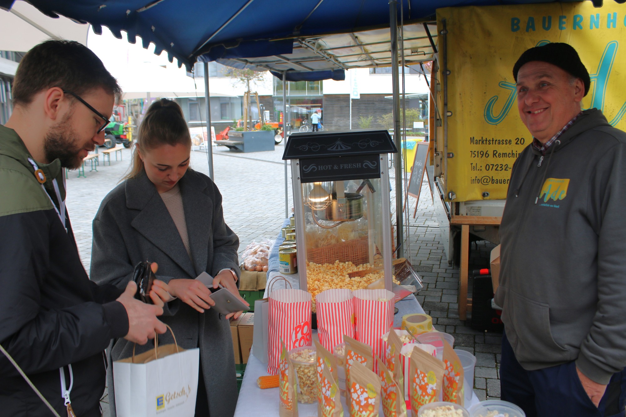 Popcorn-Stand auf einem Markt, drei Personen interagieren und verkaufen Snacks.