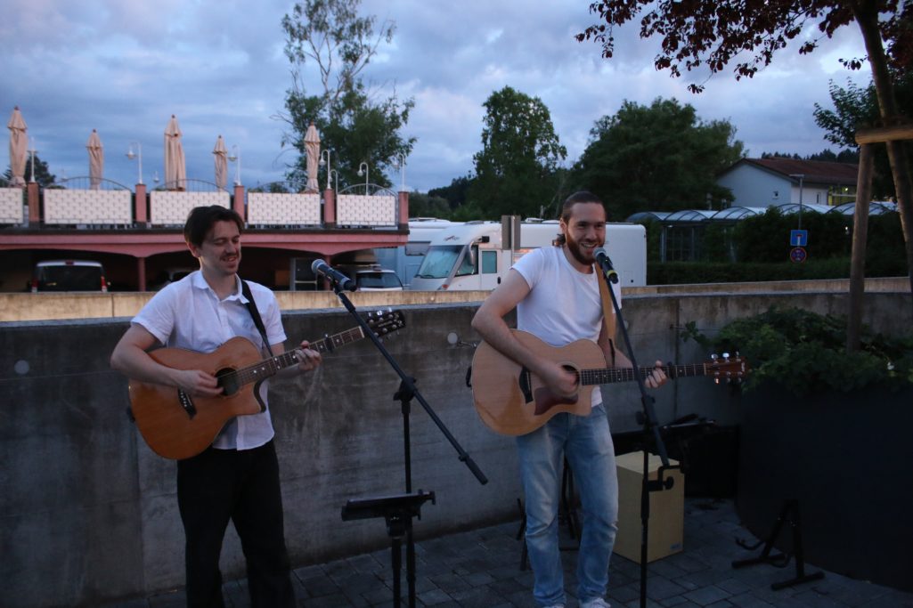 Zwei Musiker spielen akustische Gitarren im Freien bei Dämmerung.