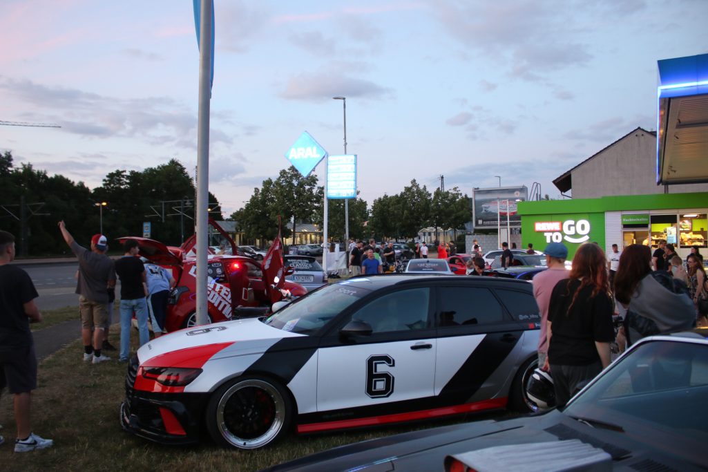 Sportliche Autos parken auf einem Treffen bei Sonnenuntergang, zahlreiche Zuschauer sind da.