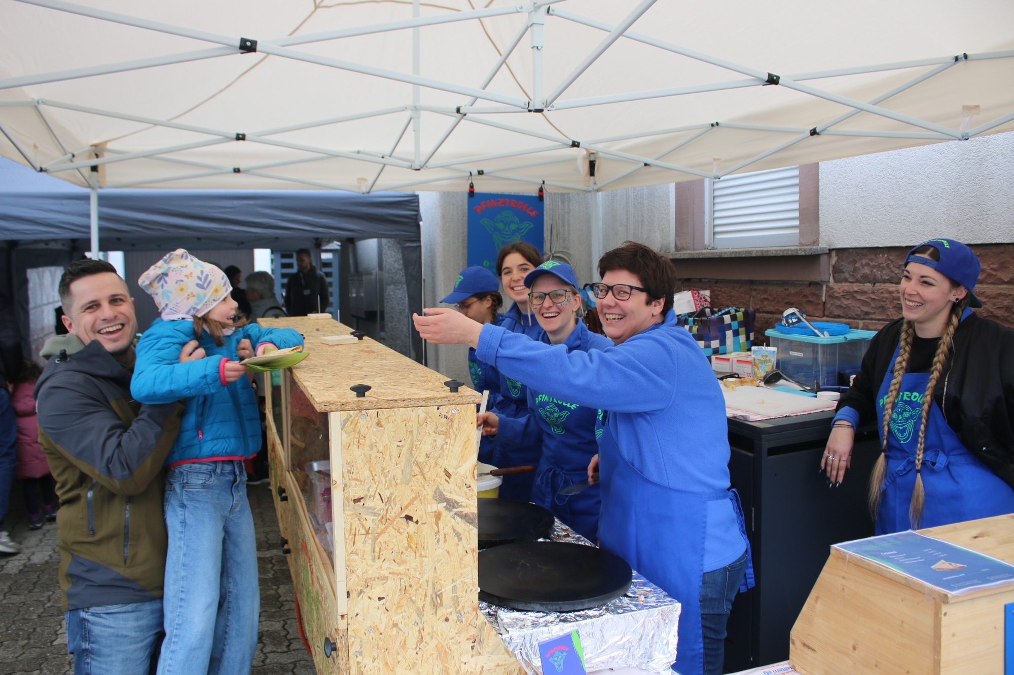 Eine Gruppe von Menschen lächelt und arbeitet an einem Stand unter einem Zelt.