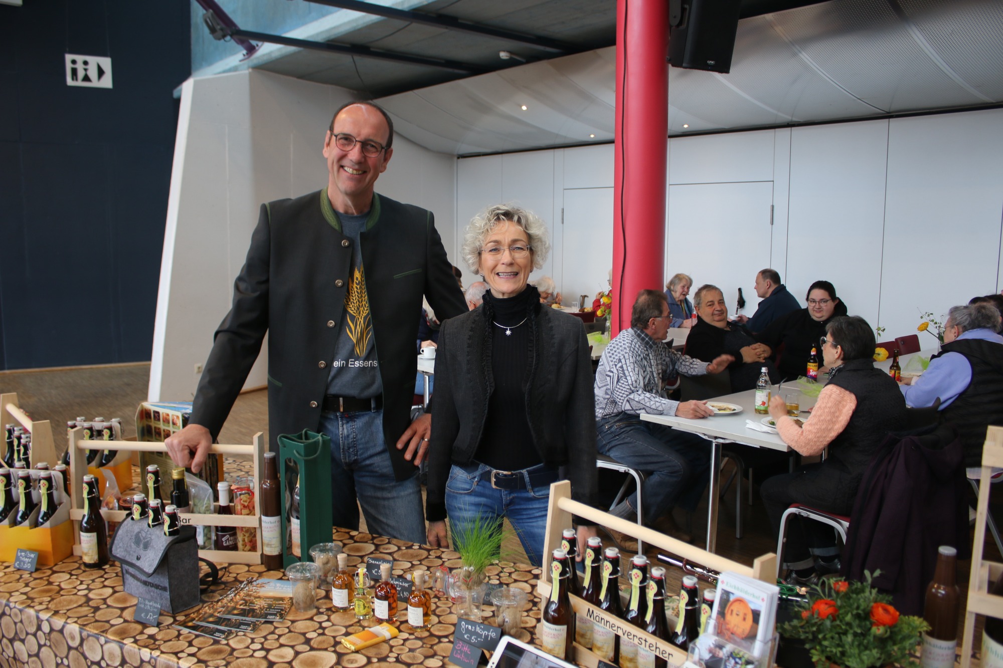 Zwei Personen stehen an einem Marktstand mit regionalen Getränken und Dekoration.