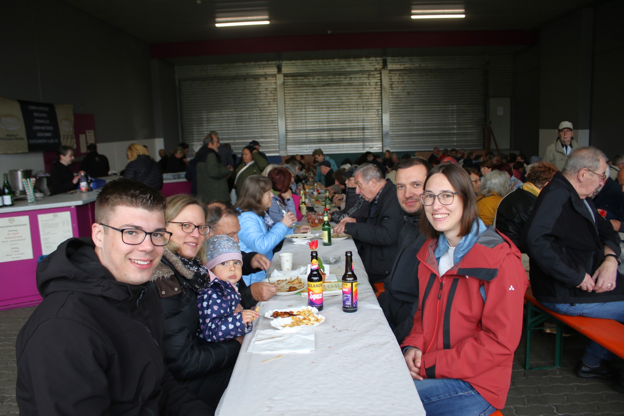 Eine Gruppe von Menschen, die an einem langen Tisch zusammen essen und lächeln.