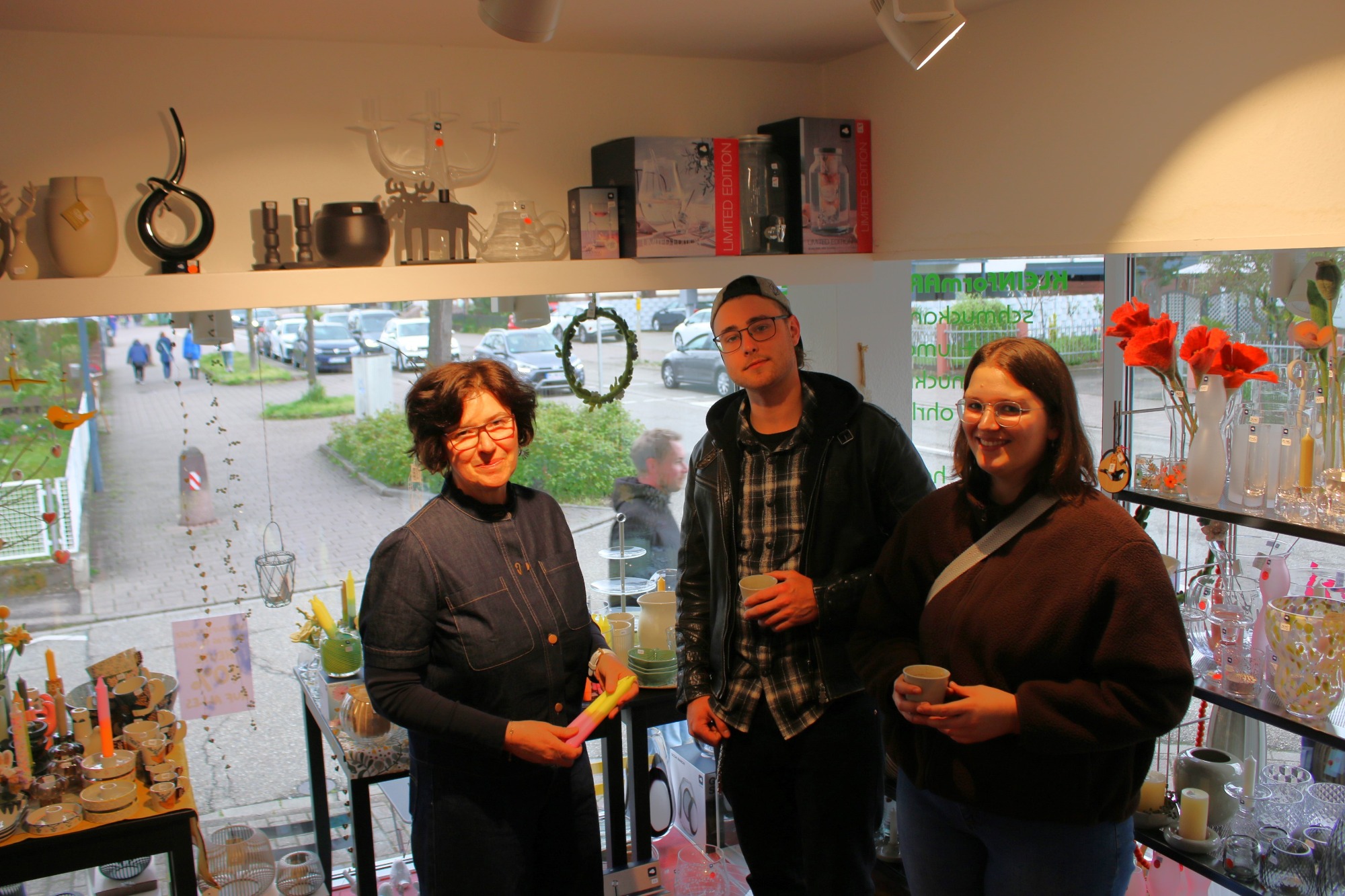 Drei Personen stehen in einem Geschäft, umgeben von Dekoartikeln und Blumen.