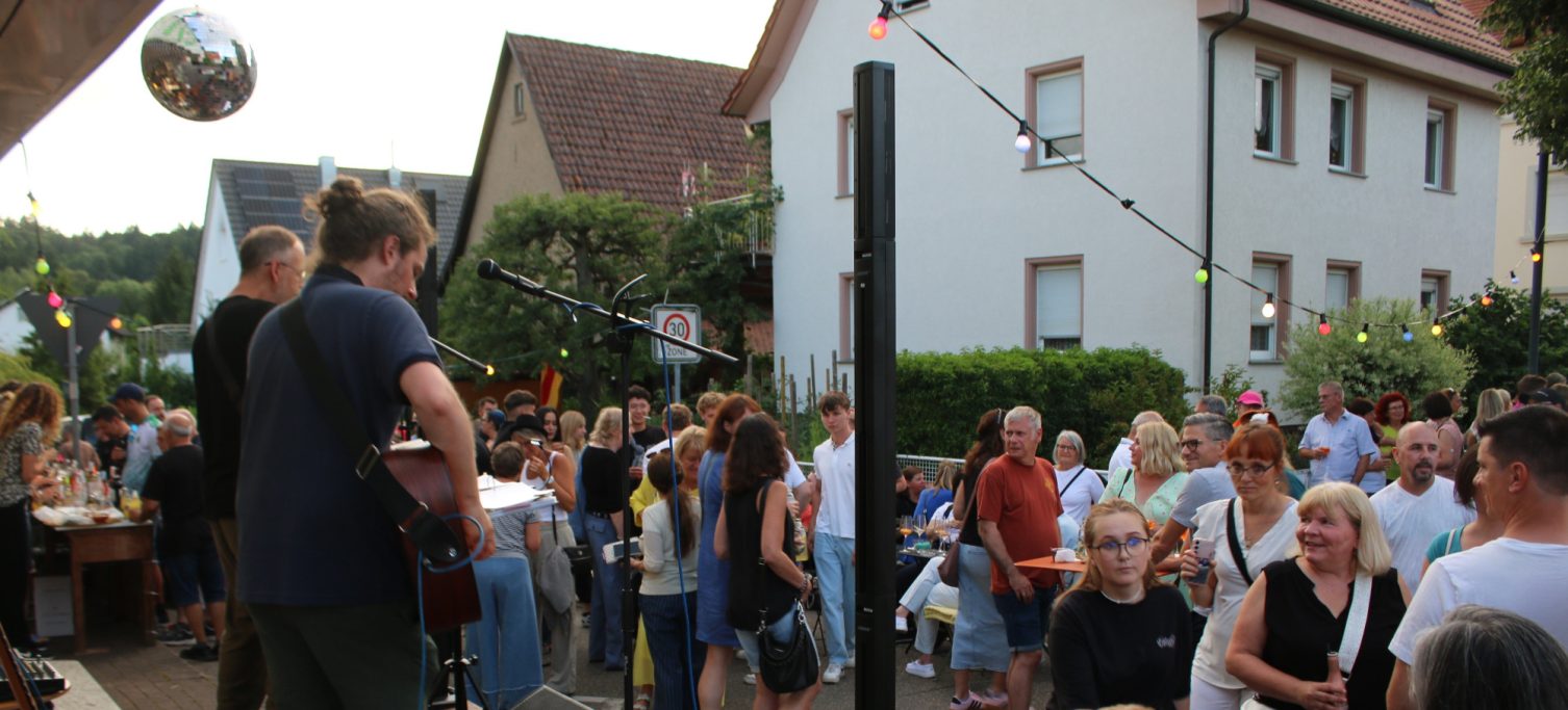 Menschenmenge bei einem Straßenfest, ein Musiker spielt Gitarre im Hintergrund.