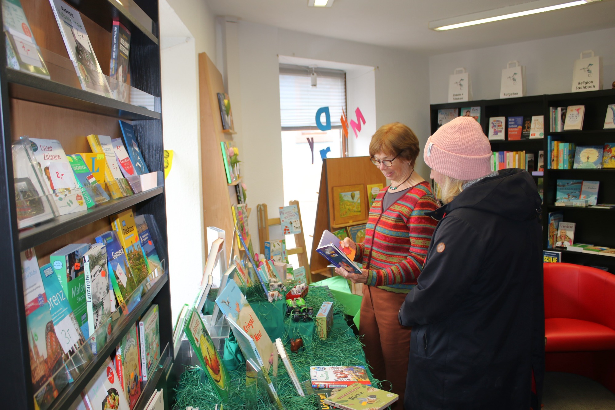 Zwei Personen in einer Bibliothek betrachten Bücher und stehen vor einer bunten Buchpräsentation.