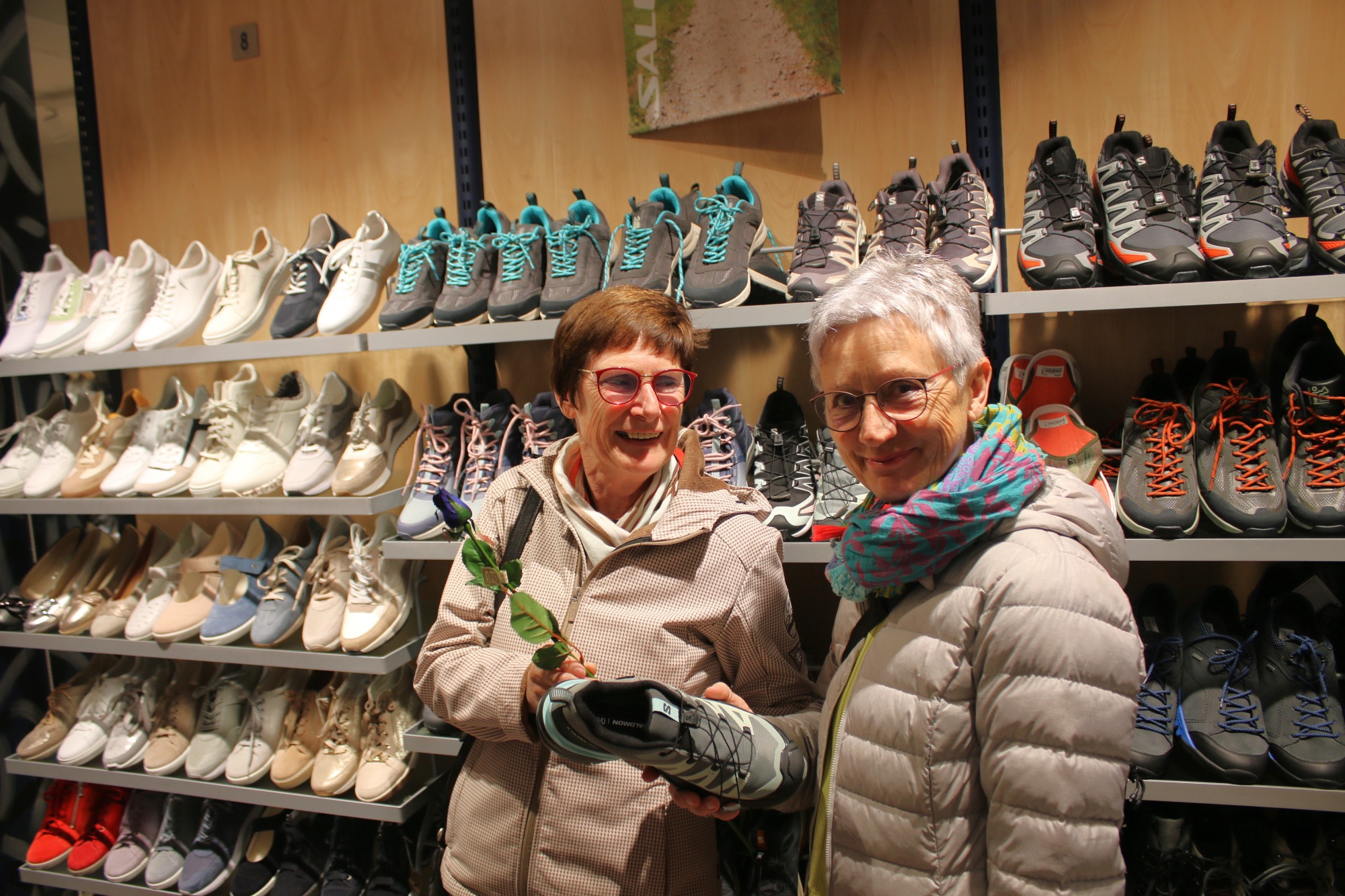 Zwei Frauen in einem Schuhgeschäft, eine hält einen Schuh, Regale mit Schuhen im Hintergrund.