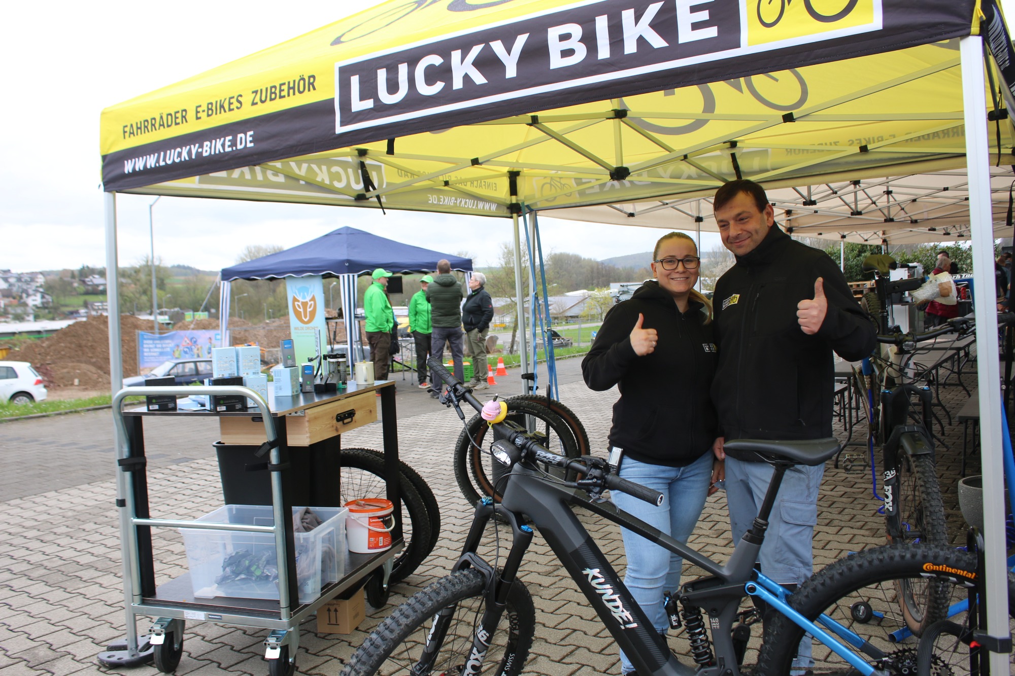 Zwei Personen zeigen Daumen hoch unter einem "Lucky Bike"-Zelt bei einer Fahrradausstellung.
