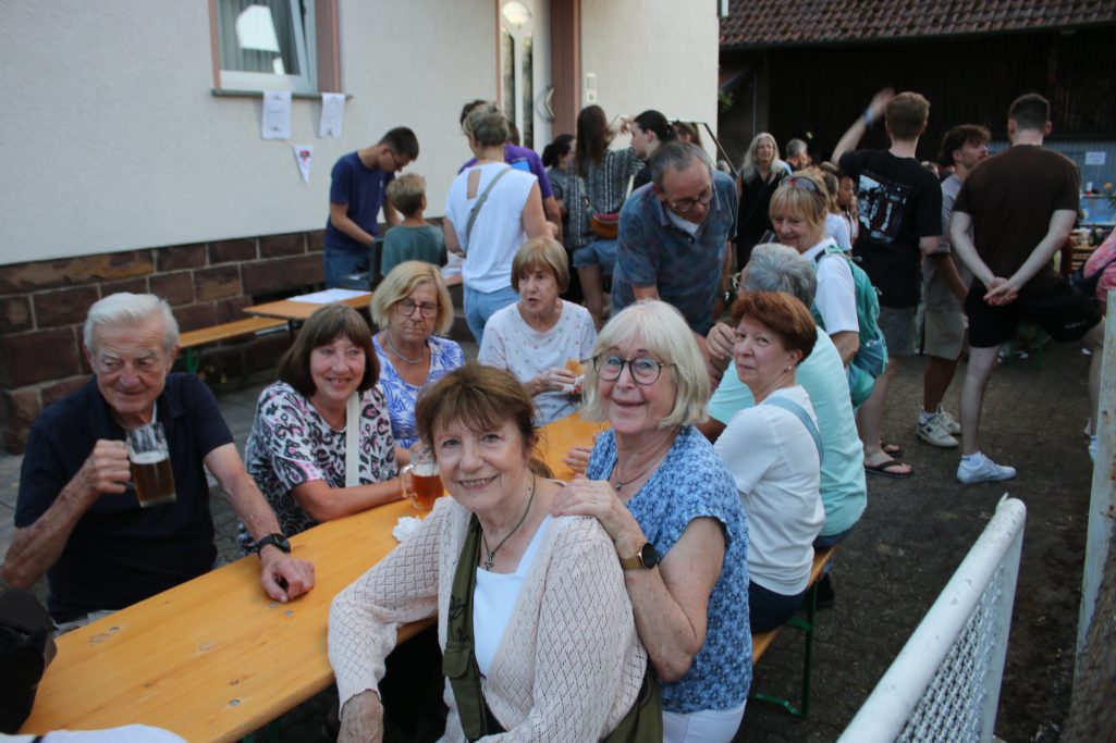 Gruppe von Menschen sitzt an Tischen und genießt eine gesellige Atmosphäre im Freien.