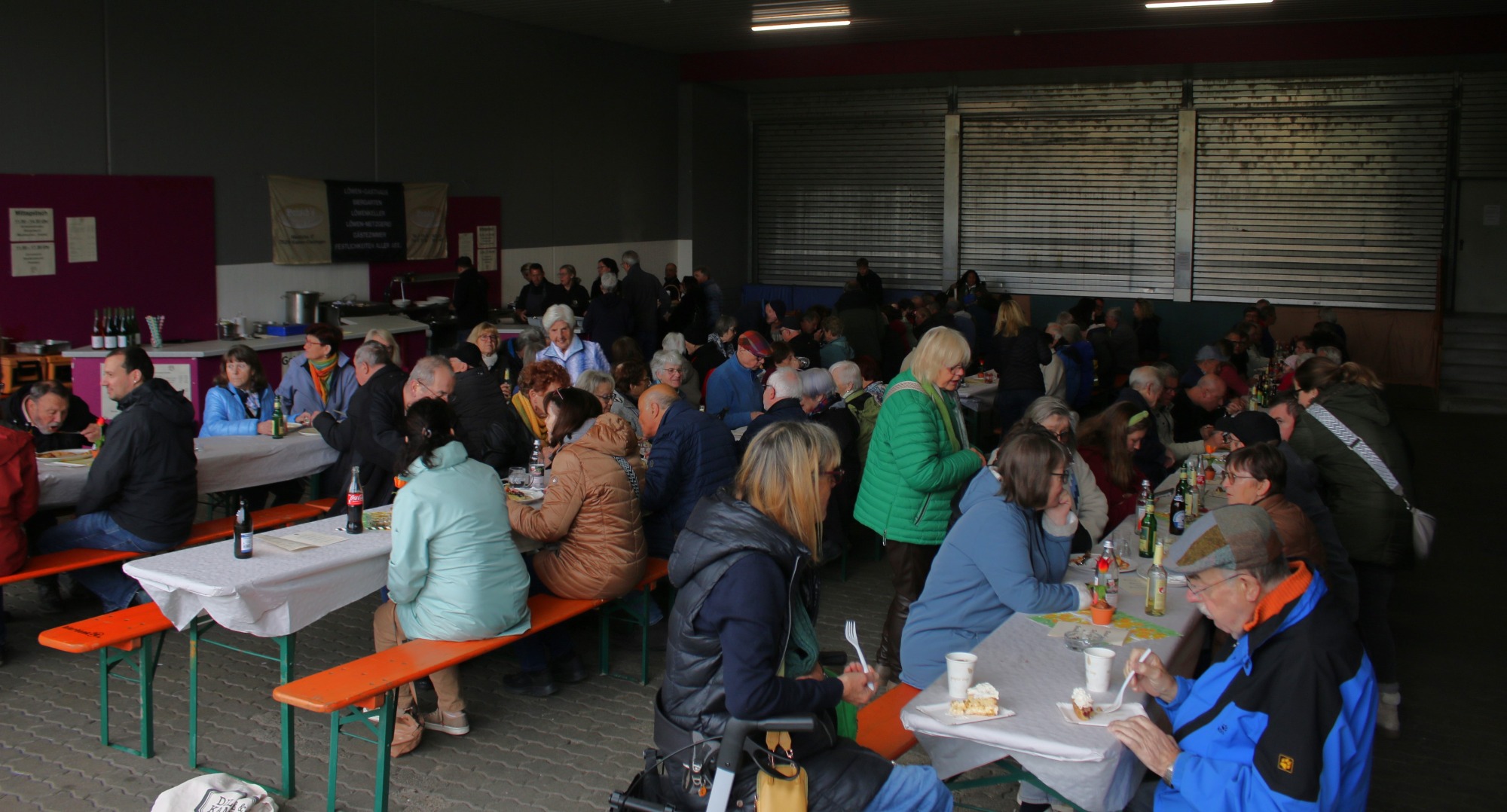Gruppenszenen in einem Raum mit vielen Menschen, die an Tischen sitzen und sich unterhalten.