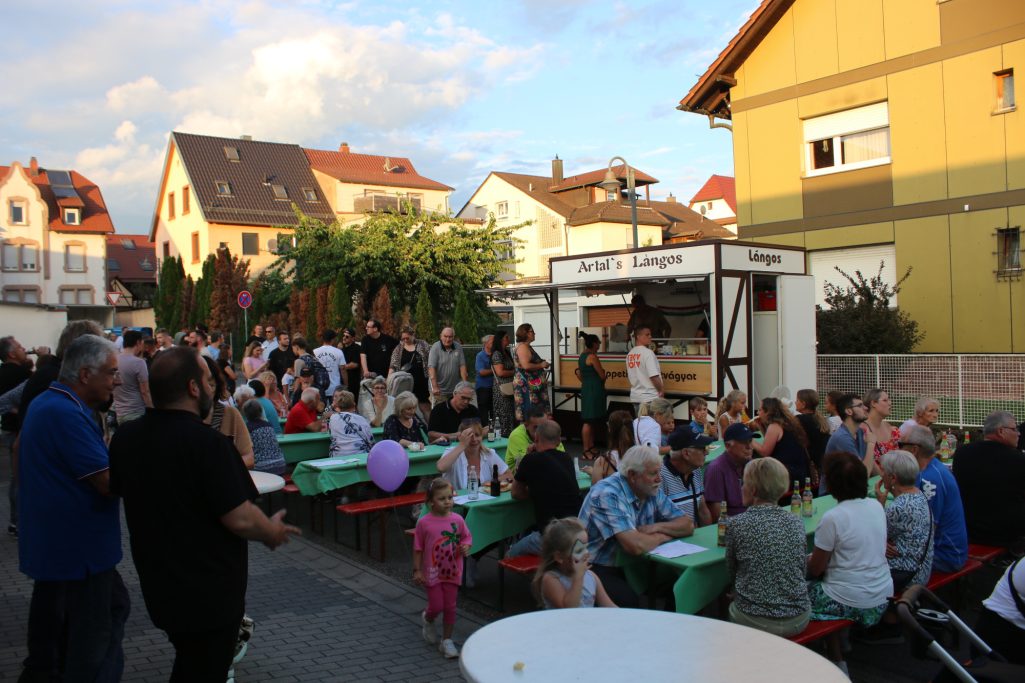 Menschen feiern eine Veranstaltung im Freien mit Ständen und Tischen auf einer Straße.